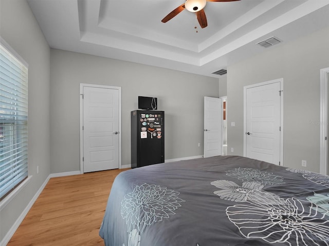 bedroom featuring multiple windows, hardwood / wood-style floors, a tray ceiling, and ceiling fan