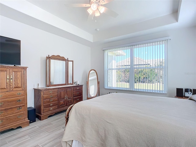 bedroom featuring ceiling fan, light wood-type flooring, and a raised ceiling