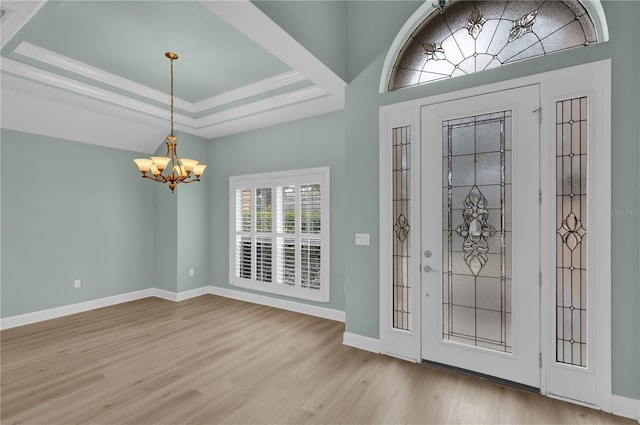 foyer entrance with a tray ceiling, a chandelier, and light wood-type flooring