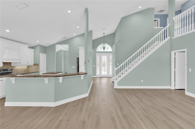 kitchen with tasteful backsplash, light hardwood / wood-style flooring, high vaulted ceiling, white cabinets, and dark stone counters