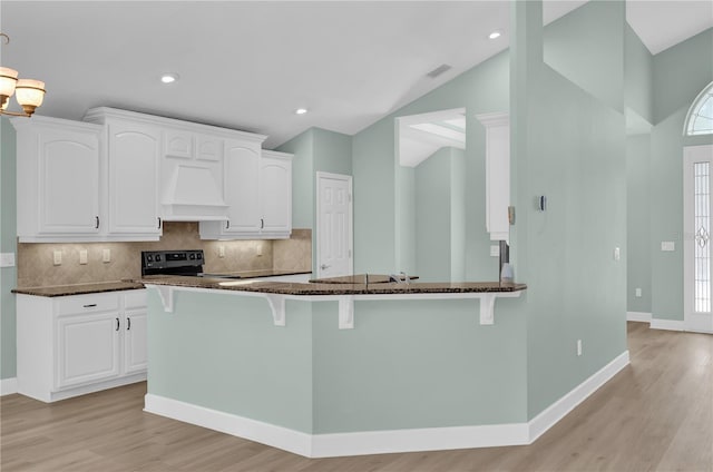 kitchen featuring premium range hood, white cabinetry, electric range, lofted ceiling, and dark stone countertops