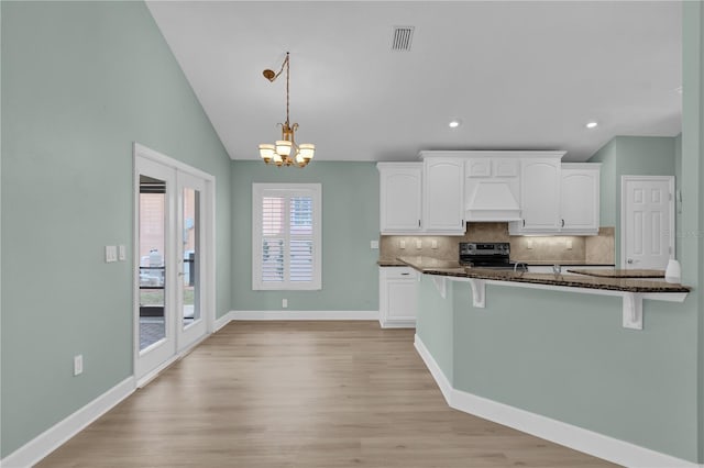 kitchen with dark stone countertops, premium range hood, pendant lighting, white cabinetry, and range with electric stovetop