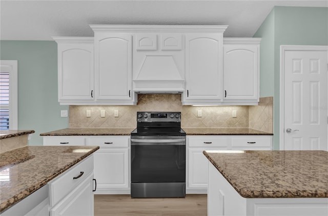 kitchen featuring premium range hood, white cabinets, dark stone counters, and stainless steel electric stove