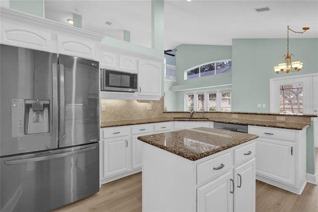 kitchen featuring white cabinetry, kitchen peninsula, appliances with stainless steel finishes, decorative backsplash, and dark stone countertops