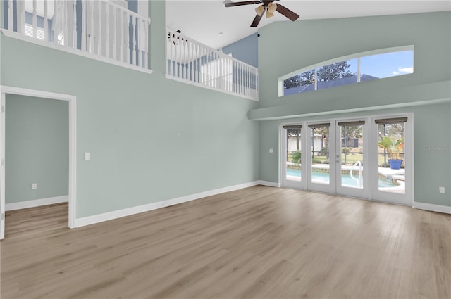 unfurnished living room with ceiling fan, french doors, a towering ceiling, and light wood-type flooring