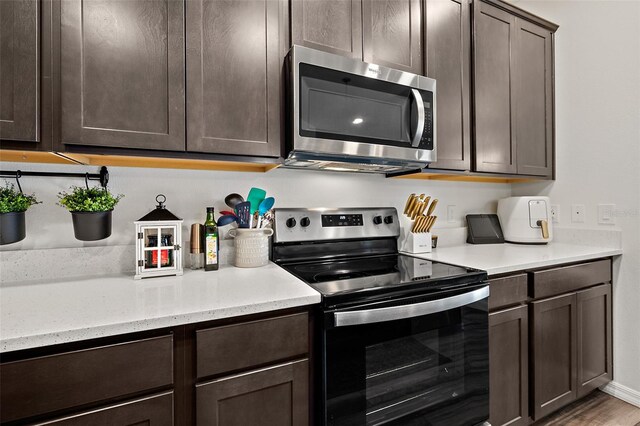 kitchen featuring appliances with stainless steel finishes, dark brown cabinets, hardwood / wood-style floors, and light stone counters