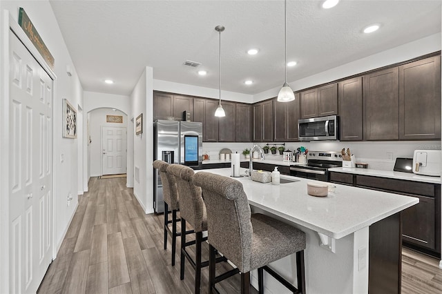 kitchen with hanging light fixtures, sink, stainless steel appliances, and dark brown cabinetry