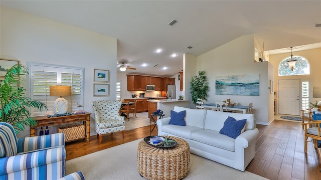 living room featuring ceiling fan with notable chandelier, light wood-type flooring, and vaulted ceiling