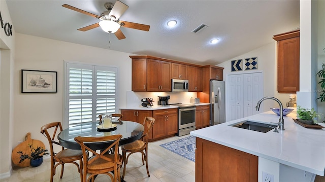 kitchen with vaulted ceiling, kitchen peninsula, sink, appliances with stainless steel finishes, and a textured ceiling