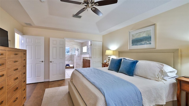 bedroom with a tray ceiling, ensuite bathroom, dark hardwood / wood-style flooring, and ceiling fan