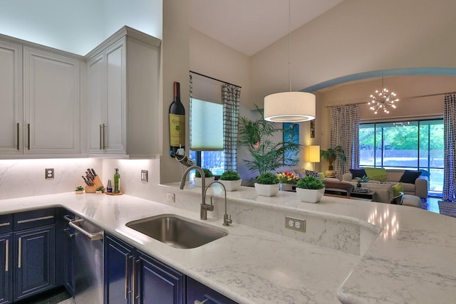 kitchen featuring decorative light fixtures, stainless steel dishwasher, sink, light stone countertops, and blue cabinets