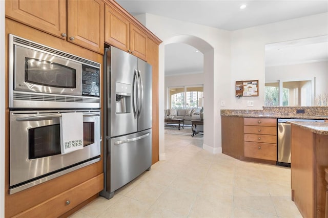 kitchen featuring light tile patterned flooring, stainless steel appliances, ornamental molding, and stone countertops