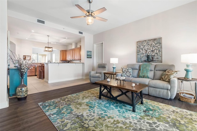 living room with a raised ceiling, light wood-type flooring, and ceiling fan