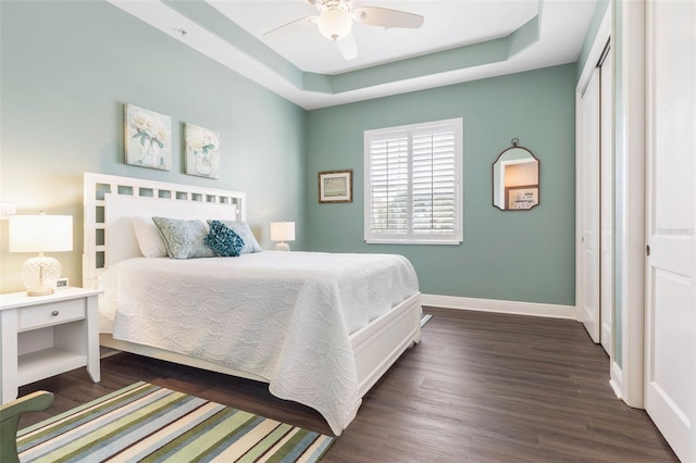 bedroom featuring a raised ceiling, ceiling fan, dark hardwood / wood-style flooring, and a closet