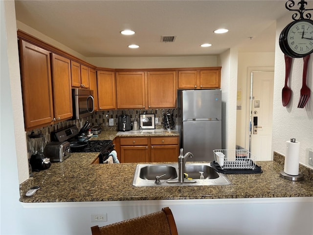 kitchen with kitchen peninsula, stainless steel appliances, decorative backsplash, dark stone countertops, and sink