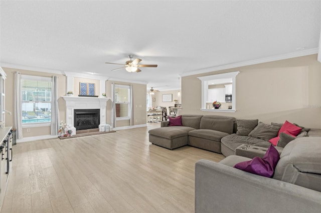 living room featuring ceiling fan, ornamental molding, light hardwood / wood-style flooring, and a large fireplace