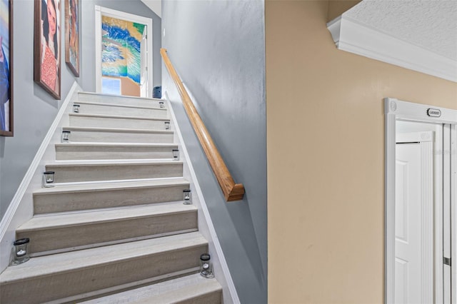 staircase featuring a textured ceiling and crown molding