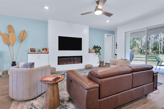 living room with a large fireplace, ceiling fan, and light hardwood / wood-style flooring