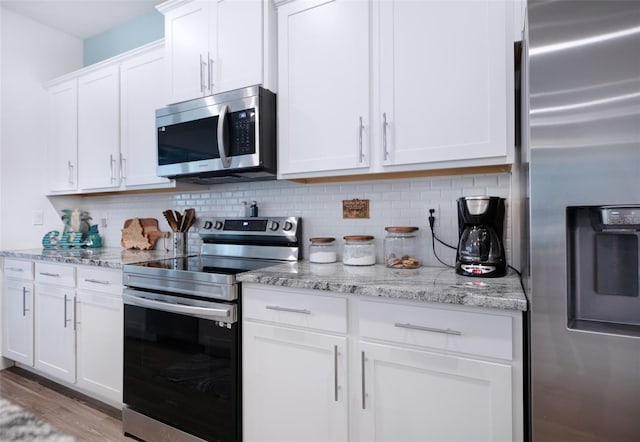 kitchen featuring white cabinetry, stainless steel appliances, light stone counters, tasteful backsplash, and light hardwood / wood-style floors