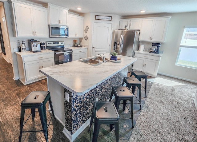 kitchen with appliances with stainless steel finishes, white cabinetry, sink, a kitchen island with sink, and a breakfast bar