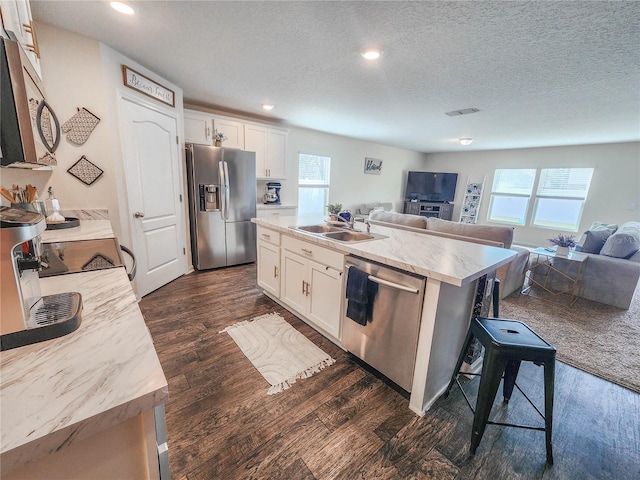 kitchen featuring an island with sink, appliances with stainless steel finishes, a textured ceiling, a wealth of natural light, and white cabinets