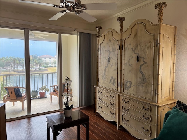 living area featuring dark hardwood / wood-style flooring, crown molding, ceiling fan, and a water view