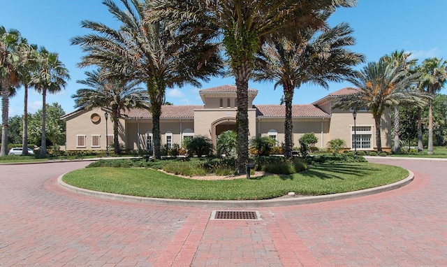 mediterranean / spanish home featuring a tile roof, a front lawn, and stucco siding