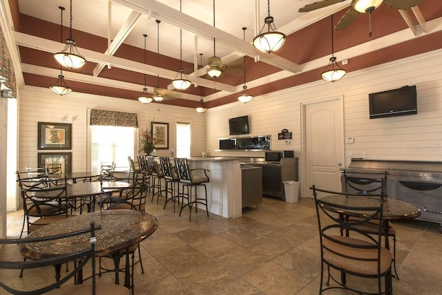 kitchen featuring wooden walls, a ceiling fan, stainless steel microwave, a kitchen bar, and decorative light fixtures