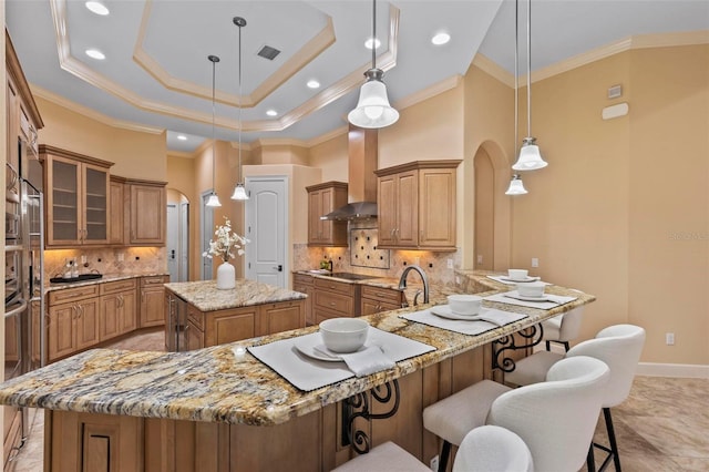 kitchen featuring tasteful backsplash, a center island, kitchen peninsula, hanging light fixtures, and wall chimney exhaust hood