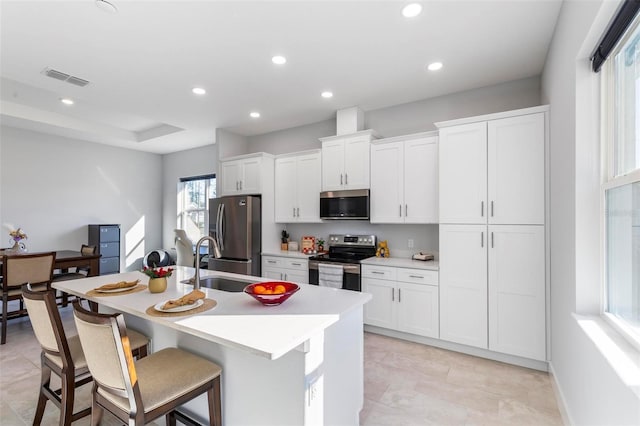 kitchen with a breakfast bar area, white cabinetry, a tray ceiling, an island with sink, and stainless steel appliances