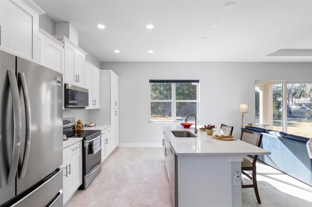 kitchen with appliances with stainless steel finishes, an island with sink, sink, white cabinets, and a kitchen bar