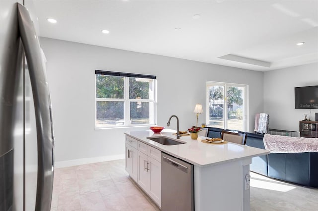 kitchen with appliances with stainless steel finishes, white cabinetry, an island with sink, sink, and a tray ceiling