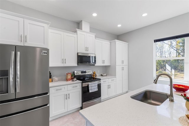 kitchen with light stone countertops, appliances with stainless steel finishes, sink, and white cabinets