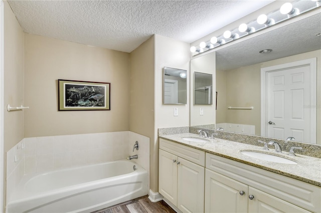 bathroom with a textured ceiling, a tub to relax in, hardwood / wood-style flooring, and vanity