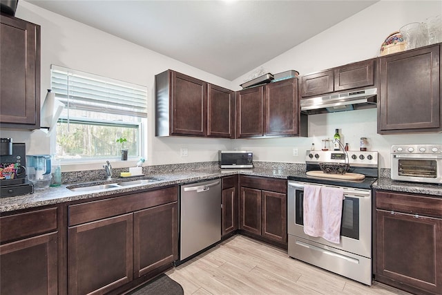 kitchen featuring lofted ceiling, appliances with stainless steel finishes, dark brown cabinets, under cabinet range hood, and a sink