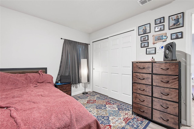 bedroom with a closet, visible vents, light wood finished floors, and baseboards