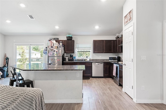 kitchen with stainless steel appliances, a healthy amount of sunlight, light wood-type flooring, and a center island