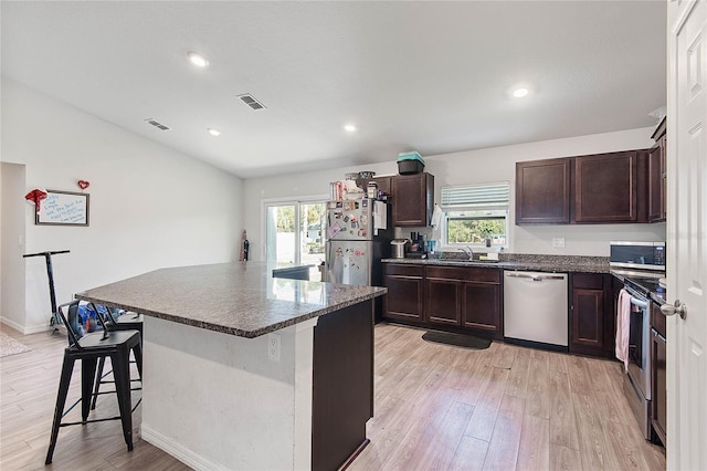 kitchen featuring light wood finished floors, a breakfast bar area, dark countertops, visible vents, and appliances with stainless steel finishes