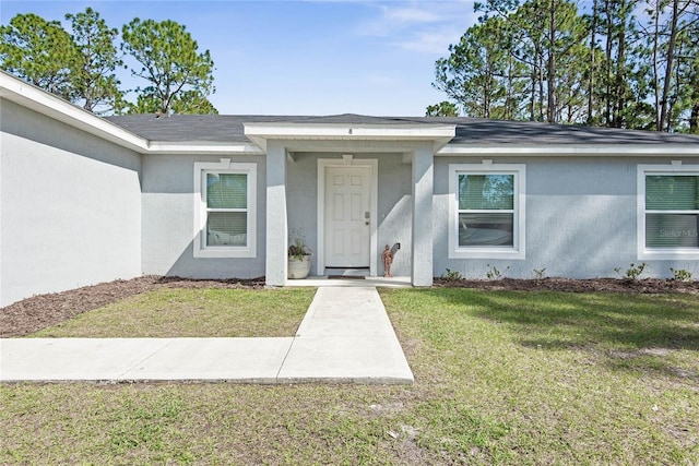 entrance to property with stucco siding, a shingled roof, and a yard