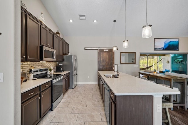 kitchen with sink, tasteful backsplash, appliances with stainless steel finishes, pendant lighting, and a barn door