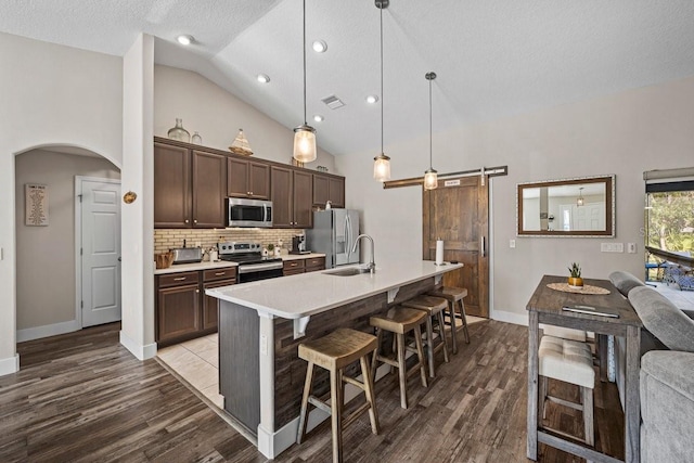 kitchen with decorative light fixtures, a breakfast bar area, backsplash, stainless steel appliances, and a barn door