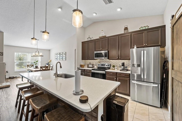 kitchen with pendant lighting, sink, stainless steel appliances, a center island with sink, and vaulted ceiling