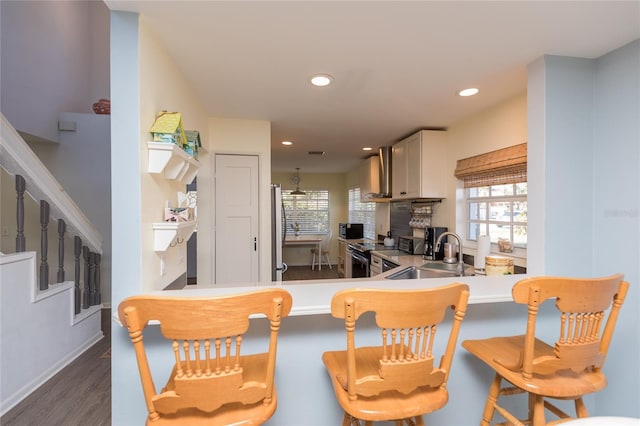 kitchen with a breakfast bar, wall chimney exhaust hood, kitchen peninsula, and sink