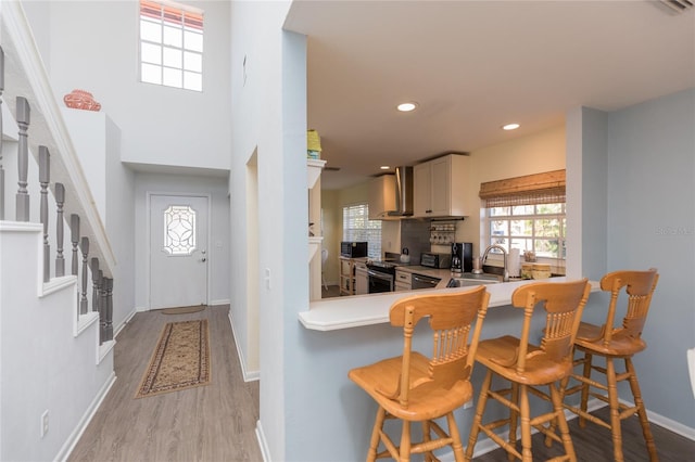 kitchen featuring wall chimney exhaust hood, sink, a breakfast bar area, light wood-type flooring, and kitchen peninsula