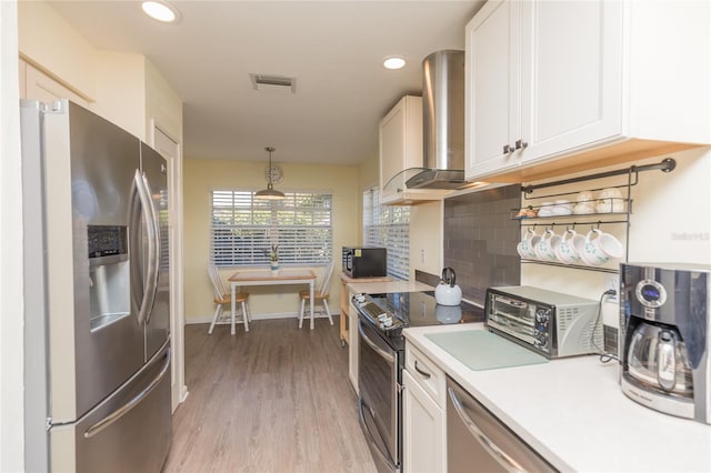 kitchen featuring wall chimney exhaust hood, hanging light fixtures, white cabinets, stainless steel appliances, and backsplash