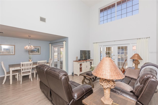 living room featuring french doors, a towering ceiling, an inviting chandelier, and light wood-type flooring