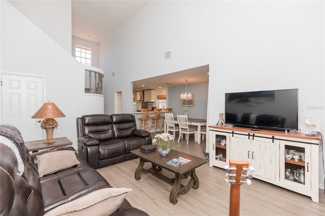 living room with a towering ceiling, an inviting chandelier, and light hardwood / wood-style flooring