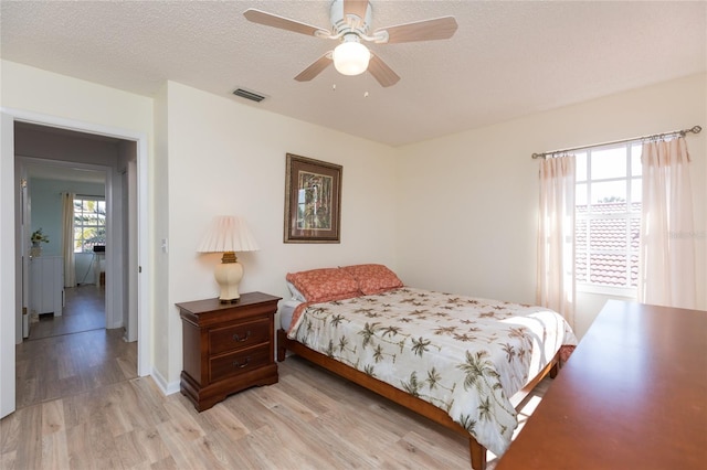 bedroom featuring multiple windows, a textured ceiling, light hardwood / wood-style floors, and ceiling fan