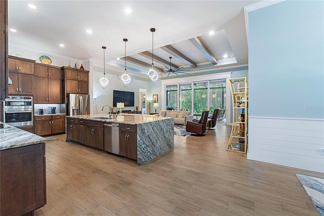 kitchen featuring sink, a large island with sink, appliances with stainless steel finishes, pendant lighting, and light stone countertops