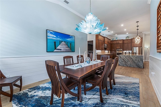 dining space with a chandelier, ornamental molding, light hardwood / wood-style floors, and vaulted ceiling